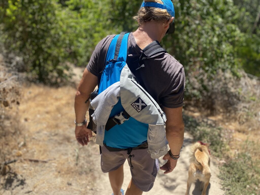 Man wearing an X-over bag is hiking with his dog